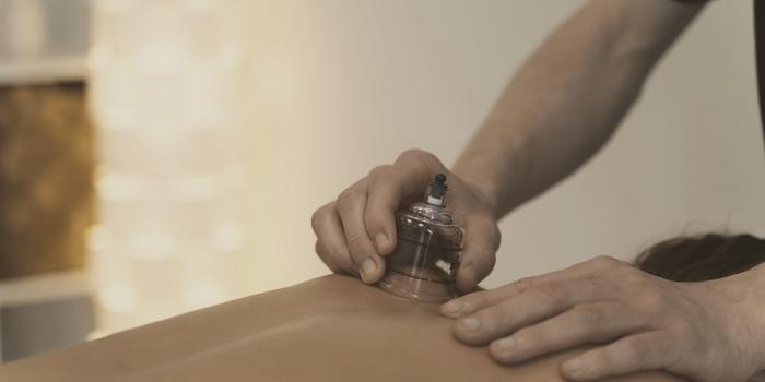 A glass cup being placed on a back, steadied by the therapist's other hand